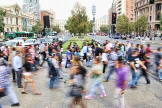 Colourful city street scene with many people rushing to cross a busy road