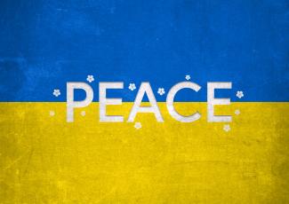 The white words of peace are written over the blue and yellow Ukraine flag surrounded by white flowers